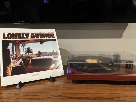 On the left standing up is the album sleeve for Lonely Avenue, by Nick Hornby and Ben Folds.  It features a picture taken inside of a van or RV,  as it pulls into an airport.  On the right, my record player spins a black record.