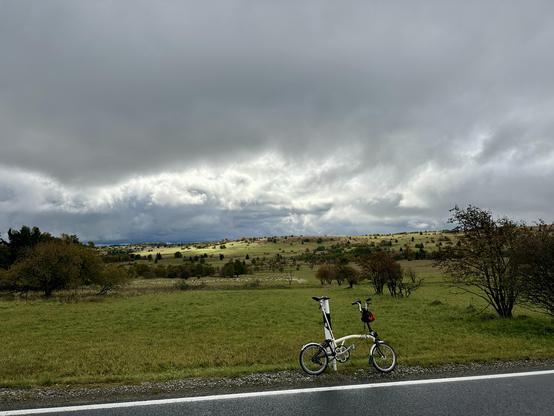 Brompton lehnt am Straßenrand. Nasses Herbstwetter. Hochebene mit Rhön-typischen freien Flächen mit einzelnen Bäumen und Büschen. Schafe ganz klein im Hintergrund.