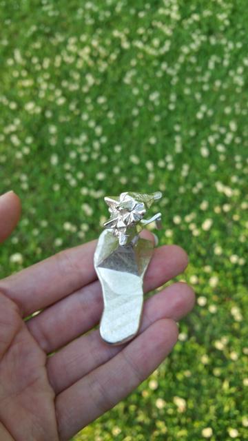 Close up of a hand holding an experimental piece of cast pewter on a clover lawn.