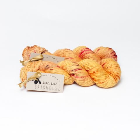 Picture shows two skeins of yarn , one behind the other, in shades of honey with red, purple and raspberry speckles.