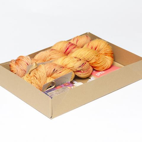Picture shows an open A4 box containing two skeins of yarn. The rest of the contents is obscured by the sides of the box.