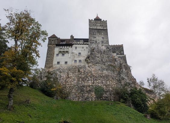 Il Castello di Bran, con le sue imponenti torri e la sua posizione in cima a una scogliera rocciosa, evoca un'atmosfera che si adatta perfettamente a una storia come quella di "Frankenstein Junior". 
L'Esterno: La struttura medievale gotica, con le sue torrette e il tetto a punta, potrebbe facilmente essere la dimora del Barone Frankenstein. Le pareti di pietra grigia e le finestre piccole e squadrate suggeriscono un luogo isolato e misterioso, dove esperimenti scientifici bizzarri potrebbero aver luogo lontano da occhi indiscreti.
L'Atmosfera: La fortezza, che si erge su un'altura rocciosa, sembra un luogo difficile da raggiungere, proprio come il castello del film. Si può quasi immaginare Igor che si aggira per i cortili, o il Barone che si affaccia da una delle finestre per contemplare la campagna della Transilvania.
Gli Interni: Anche se l'immagine non li mostra, il castello ha 57 stanze, scale a chiocciola e cunicoli. Questi labirintici passaggi sarebbero l'ambiente ideale per nascondere un laboratorio segreto o per ospitare personaggi eccentrici come Frau Blücher.