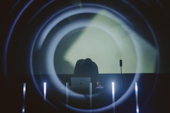 Photo of a man performing electronic music live with a laptop, with circular lights flaring around him.