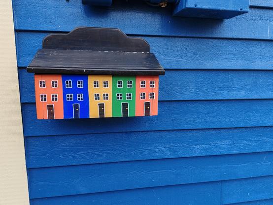 Picture of a house letterbox representing 4 house fronts viewed face on, each one painted a different vivid colour.