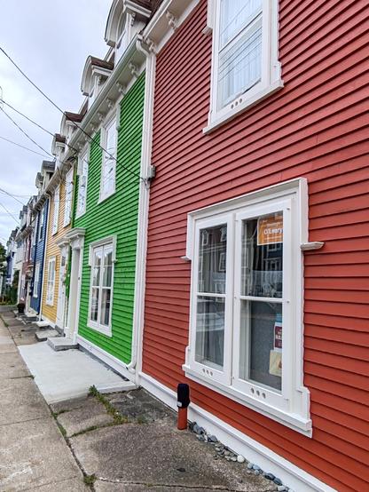 Picture of an angular view along the fronts of four traditional, shiplapped, terraced houses, each one painted a different, vivid colour.
