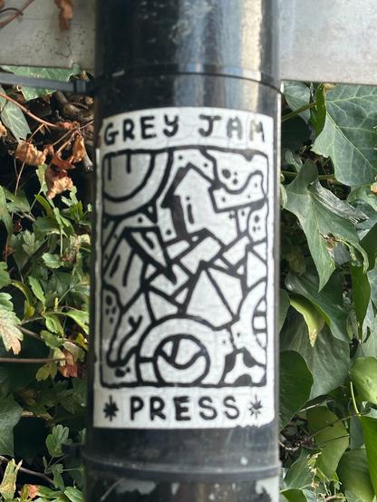 a sticker on a pole with an abstract line-art design and the text GREY JAM PRESS