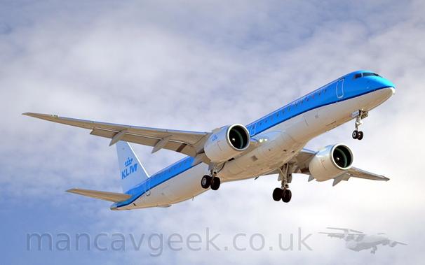 Low side view of a twin engined jet airliner flying from left to right at a very low altitude, with undercarriage lowered and flaps extended from behind the wings, suggesting it is about to land.
The plane is mostly light blue, with a white lower fuselage, separated by a thin, dark blue stripe running along the body, sweeping up slightly over the wings.
There are white "KLM CityHopper" titles on the upper forward fuselage, with blue "KLM" titles under a stylised blue crown on the white tail, and in a smaller form on the sides of the white engine pods.
There is blue text "NXV-158" on the open nose-wheel doors.
Thin fluffs of white cloud with patches of blue sky fill the rest of the frame.