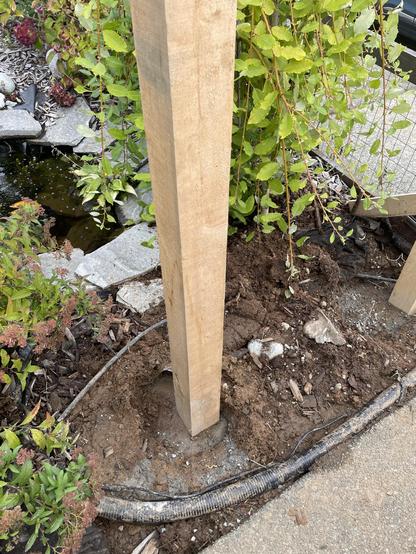 A picture of a post in the ground near the end of a pond. This is before the front gate was completed. You can see that the ground has been fully disturbed. There is not much left of the outlet that used to have rocks at the end of the pond. There are a few bushes around The Post as well.