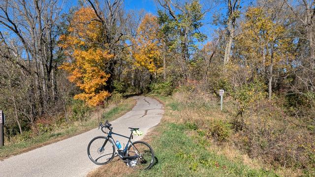 Blue and black Roubaix bicycle parked on the Douglas State Trail at Whitebridge Road looking North with a couple trees with bright yellow leaves against the blue sky.