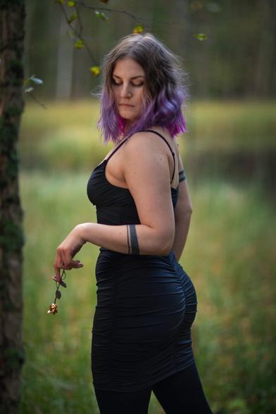 A finnish woman wearing a tight black dress posing in front of a pond in an autumn forest holding a metallic rose with her eyes closed