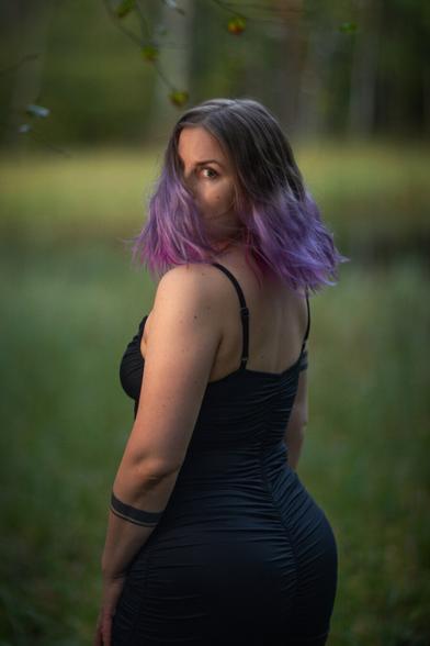 A finnish woman wearing a tight black dress posing in front of a pond in an autumn forest