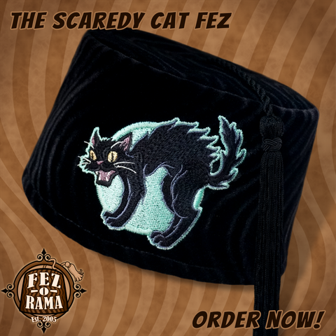 Black velvet tasseled fez cap with an embroidery featuring a hissing black cat with an arched back in front of a pale green full moon.