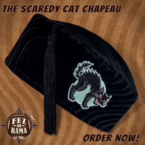 Black velvet tasseled cap with an embroidery featuring a hissing black cat with an arched back in front of a pale green full moon.