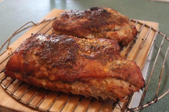 Two medium pieces of BBQ smoked pork loin rest on the circular grate, which is on a wood cutting board.