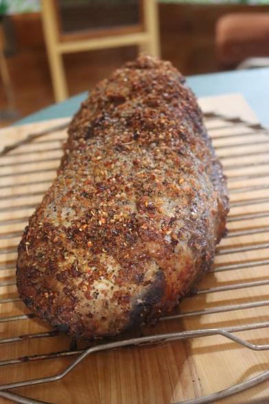 The smoked eye of round rests on a circular grate, which is on a wooden cutting board.
