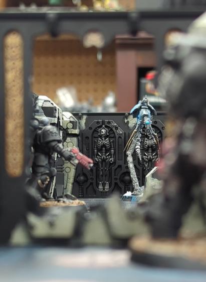 Warhammer miniatures set up in the middle of a game of Kill Team. Looking through a breached wall in the Necron Tomb World: a Deathwatch Space Marine prepared to gun down a Mention Canoptek Warrior.