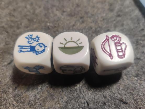 Three dice with pictograms on their faces. the faces show a person waking up, a sunset and a bow and arrow.