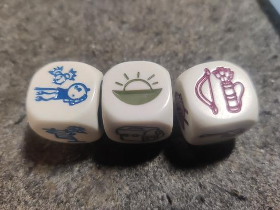 Three dice with pictograms on their faces. the faces show a person waking up, a sunset and a bow and arrow.