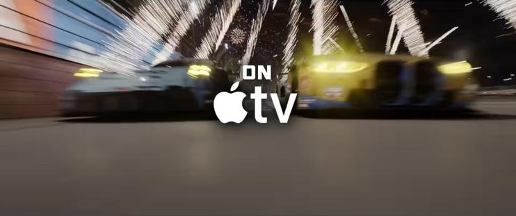 Two racing cars speed side by side under bright fireworks at night with the Apple TV logo and the words “ON Apple TV” displayed in the center.