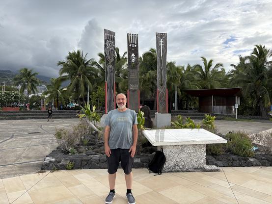 An old white man standing in front of a monument with trees in the background