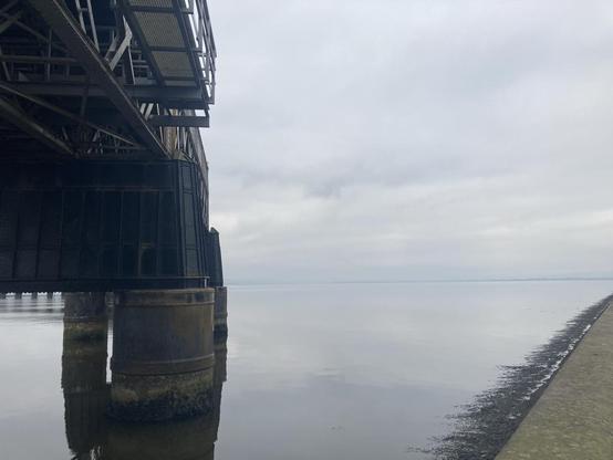 View of the rail bridge on a grey misty morning with the water still at high tide reflecting waves of the cloud