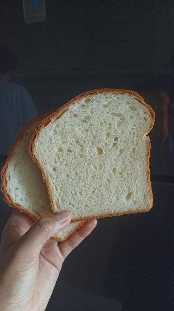 My hand, holding up two slices of bread, like one holds cards, against a shiny black background. You can see the airy, fluffy crumb with the edge of golden brown crust.