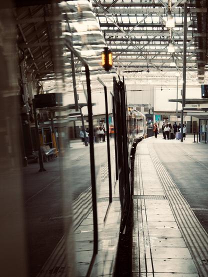 Looking at the train alongside the platform while entering it. The windows reflect a scene from the platform, people walking, lights, the ceiling, a bench that's out of frame.