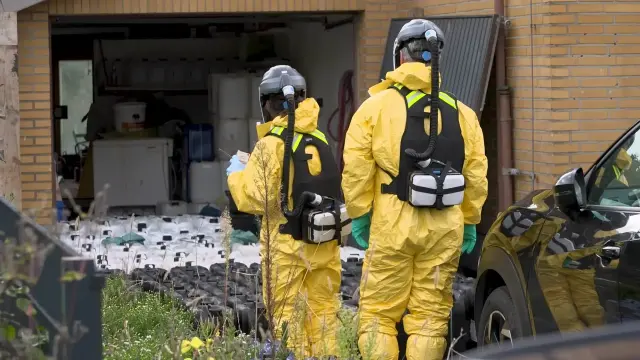 Bild: Zwei Personen in gelben Schutzanzügen mit Atemmasken betreten ein Gebäude.