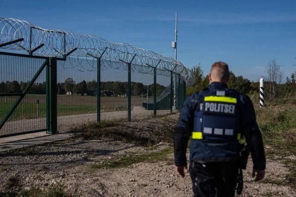 An Estonian border police officer re-enters a gate in a security fence marking the Estonian-Russian border in Vinski, Estonia, October 2025