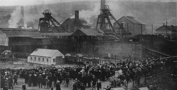 Crowds await news at the Universal Colliery, Senghenydd. By Unclear. There are five photographs on the page, and the newspaper states &quot;Photographs by Topical, CN, Illustrations Bureau and Record Press&quot; - The Senghenydd Colliery Disaster of 14 October 1913. The caption in The Illustrated London News reads: &quot;After the explosion which wrecked the pit-head gear and set half the Lancaster Pit Ablaze: the pit-head at the Universal Colliery after the disaster&quot;, Public Domain, https://commons.wikimedia.org/w/index.php?curid=47036955