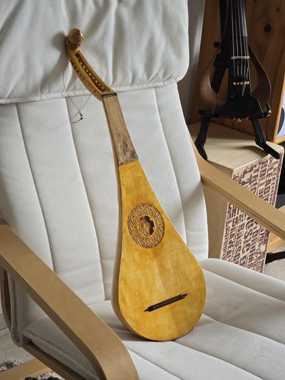 Small, pear shaped instrument with ten strings resting on a white ikea chair, Three-quarter view
