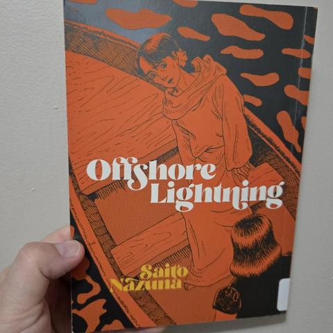 Photograph of a white person's hand holding a book, Offshore Lightning, against a light colored wall. The title is written in white in the middle with the author's name, Saito Nazuna, in yellow text in the lower left hand corner. The cover shows a woman in robes on a rowboat standing up. The entire image is in shades of orange and black. No other color on the image.