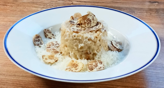Auf dem Teller eine Portion im Servierring angerichtetes Risotto mit reichlich fein gehobelten Trüffel-Scheibchen