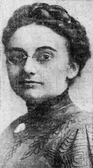 Clara Seippel, from a 1912 newspaper; a white woman with dark hair braided across the crown, wearing glasses and dark dress with a high collar