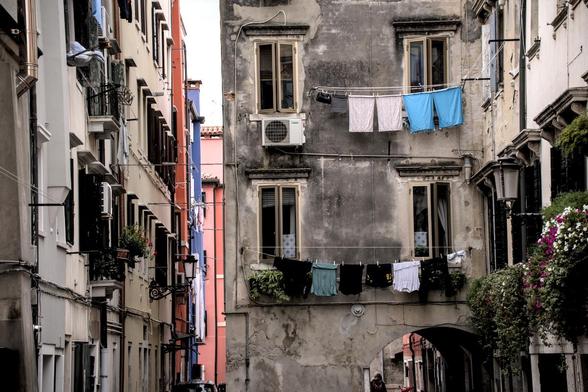 Eine Gasse mit alten Häusern und schmutzigen Fassaden. Vor den Fenstern hängt Wäsche zum Trocknen. Teilweise gibt es auch Blumenkästen mit Blumen.