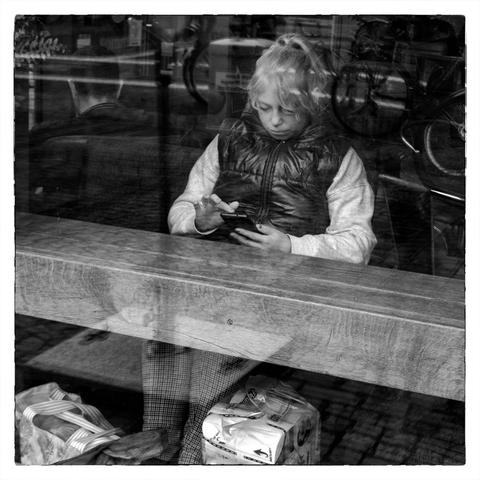 Junge Frau hinter Fensterscheibe mit Blick auf Smartphone