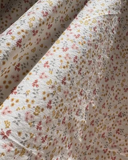 Detail view of Oolie organic cotton crib sheet with prairie ditsy pattern, showing tiny, colorful flowers printed on natural fabric.