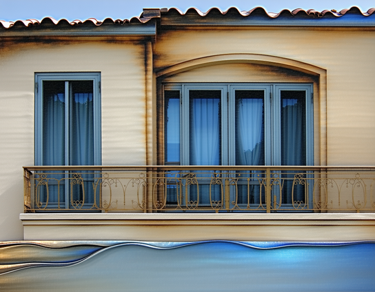 A seaside motel balcony with blue-framed windows, gold iron railings, and wave-like reflections in shades of blue and beige.