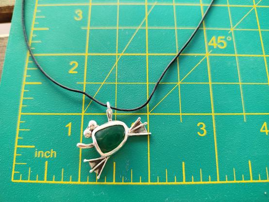 a silver frog pendant with a green semitransparent gemstone. it's on s green dimension pad
