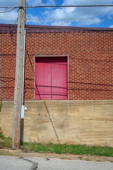 A red double door in a brick building sits 6 to 8 feet above the street with no stairs.