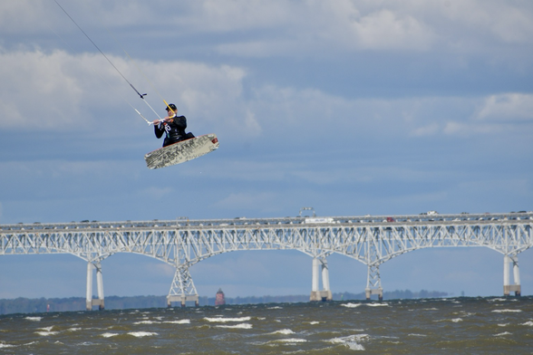 Kite surfer flying high above the water with the Chesapeake Bay Bridge in the background.