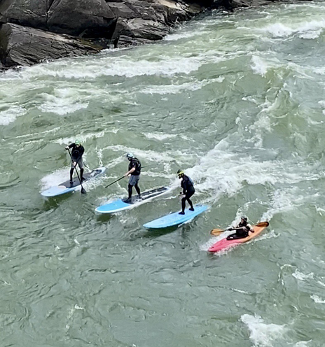 Three surfers and a kayaker lined up while surfing on the  Potomac river