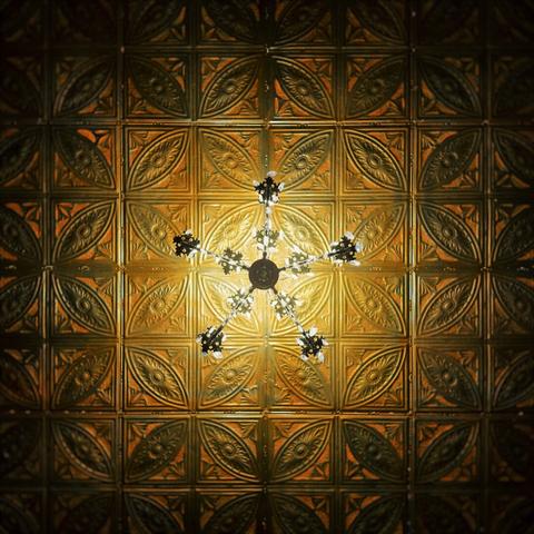 A centered chandelier casts heavy amber light onto a textured, golden-tiled ceiling.