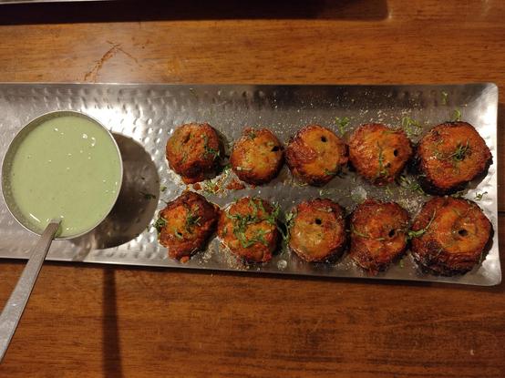 10 pieces of golden-brown mushroom tikka on a steel plate, garnished with coriander and served with a pale green mint-yoghurt chutney.