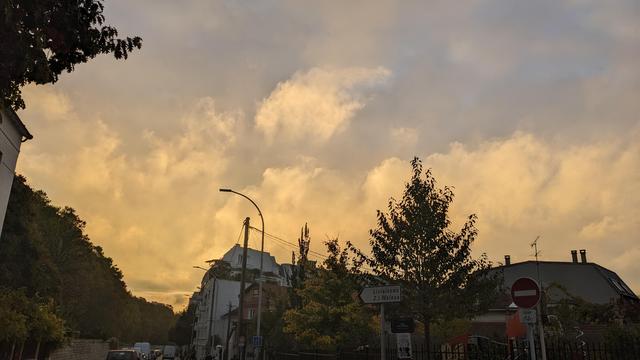Paysage urbain au lever du soleil, nuages de brume teinté de jaune-orange par le soleil et patches de ciel bleu