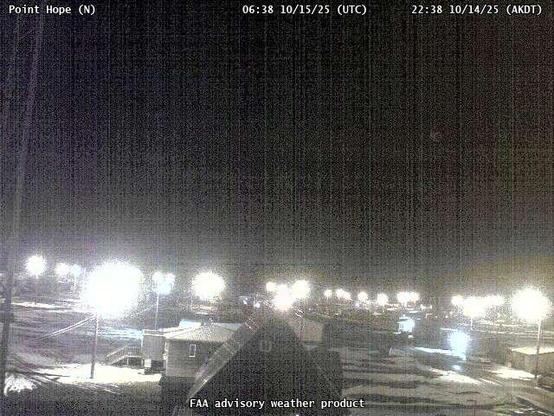 A webcam overseeing a beach with an ocean view, with a few small buildings and utility poles.