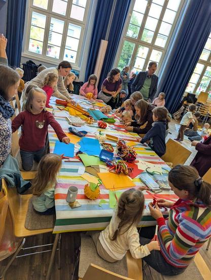 Großer Tisch an dem viele Kinder sitzen und basteln. Auf dem Tisch liegt Bastelmaterial.