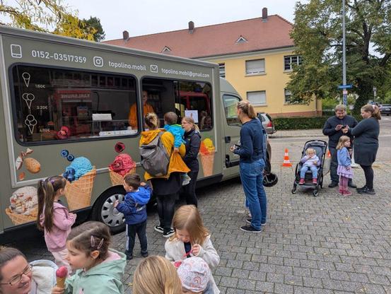 Viele eisessende Kinder vor einem Eismobil.