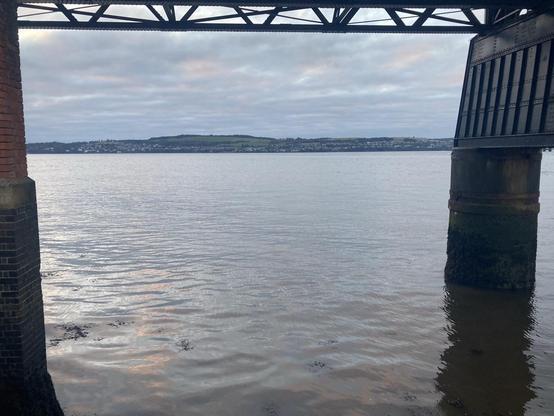 View of Tay firth framed by the rail bridge with the water rippling under grey cloudy sky
