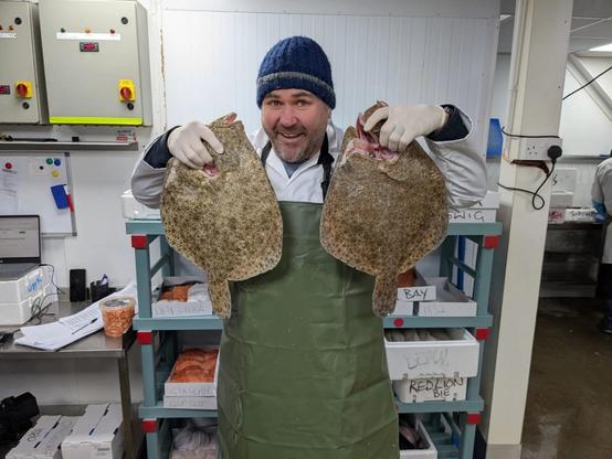 Scott Quinnell smiling while holding two large flatfish during a night shift at Swansea Fish for new S4C series.
